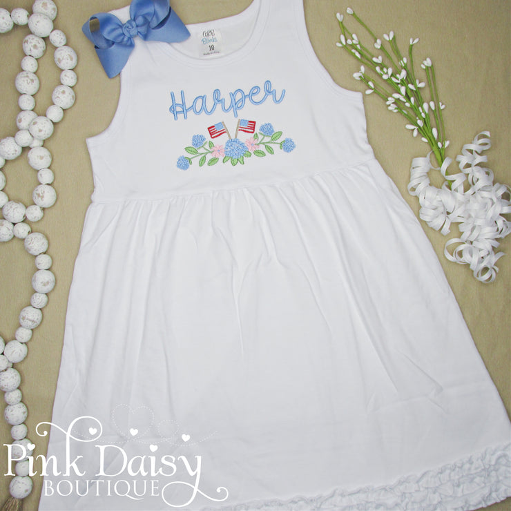 White toddler dress with personalized embroidery of name Harper in soft blue, pastel floral hydrangeas, and two small American flags. Features a sleeveless design and ruffled hem, perfect for patriotic celebrations, summer photos, and handmade holiday outfits.