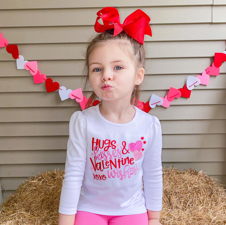 Little girl making a kissy face wearing an embroidered  Valentine's Day shirt that says, "Hugs kisses and Valentine wishes".