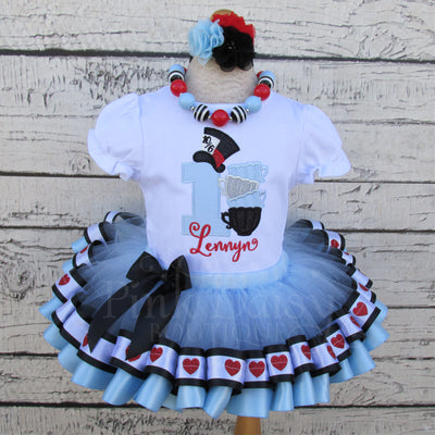 Baby girl first birthday outfit inspired by Alice in Wonderland, featuring a light blue embroidered 'Alice in ONEderland' onesie, black and blue birthday tutu, and a matching hair bow, perfect for smash cake photos, Wonderland themed birthday parties, and toddler first birthday photoshoots.